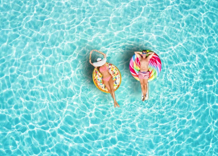 Deux personnes flottent sur des bouées gonflables dans une piscine turquoise, pendant la canicule en France