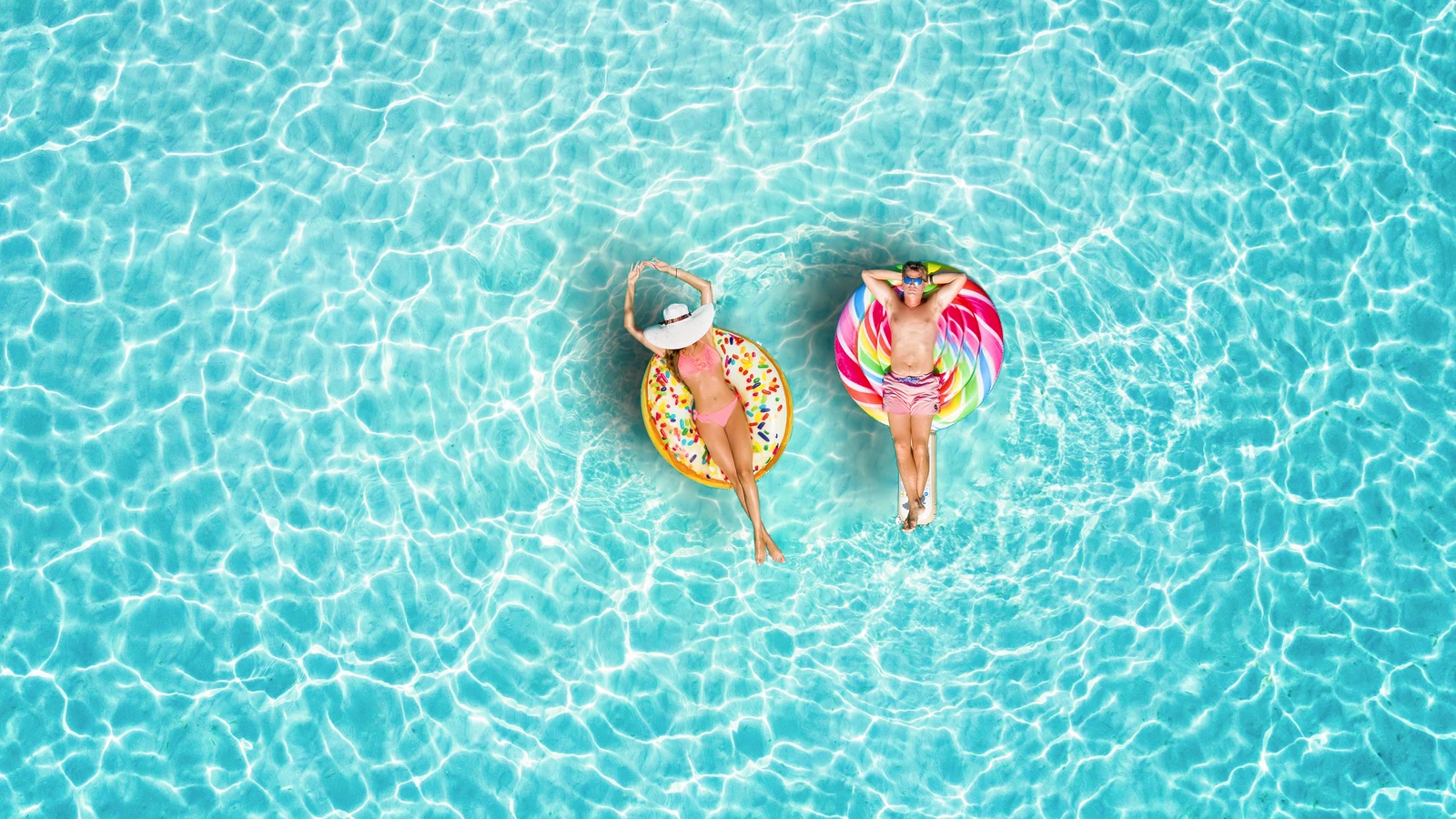 Deux personnes flottent sur des bouées gonflables dans une piscine turquoise, pendant la canicule en France